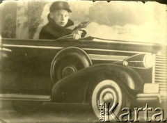 Druga połowa lat 30. do 1941, Kozienice, Polska.
Portret chłopca w makiecie samochodu.
Zdjęcie wykonane w atelier fotograficznym żydowskiego fotografa Chaima Bernemana. Przed wojną zakład mieścił się w Kozienicach na rogu ulic Warszawskiej i Maciejowickiej, przed wybuchem wojny albo już w czasie niemieckiej okupacji został przeniesiony na ulicę Lubelską 13. Cała kolekcja jest datowana na okres od drugiej połowy lat 30-tych do roku 1941, kiedy Chaim Berneman wraz z rodziną został zesłany do obozu pracy w Wolanowie. Berneman zmarł po ucieczce z obozu.
Fot. Chaim Berneman (Chaim Berman), zbiory Ośrodka KARTA