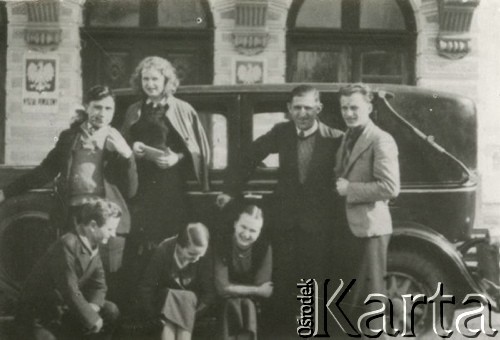 Druga połowa lat 30. do 1939, Kozienice, Polska.
Grupa maturzystów obok samochodu, w tle budynek Wydziału Powiatowego.
Zdjęcie wykonane w atelier fotograficznym żydowskiego fotografa Chaima Bernemana. Przed wojną zakład mieścił się w Kozienicach na rogu ulic Warszawskiej i Maciejowickiej, tuż przed wybuchem wojny albo już w czasie niemieckiej okupacji  został przeniesiony na ulicę Lubelską 13. Cała kolekcja jest datowana na okres od drugiej połowy lat 30-tych do roku 1941, kiedy Chaim Berneman wraz z rodziną został zesłany do obozu pracy w Wolanowie. Berneman zmarł na tyfus po ucieczce z obozu.
Fot. Chaim Berneman (Chaim Berman), zbiory Ośrodka KARTA