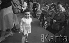 25.06.1981, Radom, Polska.
Dwie kobiety przyglądają się małemu dziecku ubranemu w jasną sukienkę i rajstopy. W tle widoczni są przechodnie.
Fot. NN, zbiory Ośrodka KARTA/Independent Polish Agency (IPA).