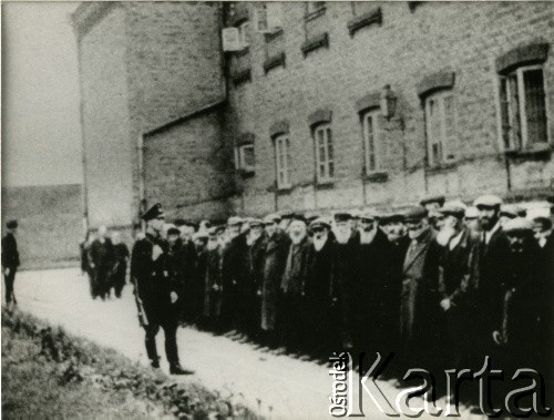 1939-1942, Płońsk, Polska.
Żydzi na dziedzińcu więziennym, pilnowani przez funkcjonariusza Einsatzkommando 3. Fotografię wykonał funkcjonariusz Einsatzkommando 3, wchodzący w skład Einsatzgruppe V, dowodzoną przez Ernsta Damzoga.  
Fot. NN, zbiory Ośrodka KARTA, przekazał Jan Ptasiński