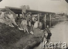 Lato 1932, Brześć nad Bugiem okolice, Polska.
Nad brzegiem Muchawca. Trzecia z lewej siedzi Irena Skorupska, nad nią stoi Ferdynand Skorupski, obok z założoną przez ramię dętką Kazik Skorupski.
Fot. NN, zbiory Ośrodka KARTA, album Ireny Skorupskiej udostępniła Agata Witerska