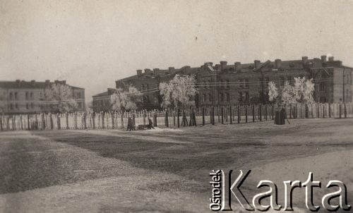 Ok. 1918, brak miejsca.
Zima, widok na budynki otoczone ogrodzeniem i znajdujące się przed nimi oszronione drzewa. Przy ogrodzeniu idzie trzech mężczyzn z wózkiem.
Fot. NN, zbiory Ośrodka KARTA, Pogotowie Archiwalne [PAF_004], udostępniła Anna Stańczykowska