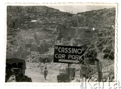 Maj 1944, Cassino, Włochy.
Miejscowość Cassino w ruinach, na pierwszym planie zwoje drutu kolczastego i tablica informująca o parkingu.
Fot. Czesław Dobrecki, zbiory Ośrodka KARTA, Pogotowie Archiwalne [PAF_015], przekazał Krzysztof Dobrecki