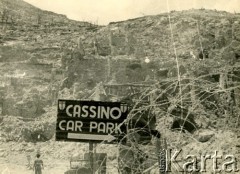 Maj 1944, Cassino, Włochy.
Miejscowość Cassino w ruinach, na pierwszym planie zwoje drutu kolczastego i tablica informująca o parkingu.
Fot. Czesław Dobrecki, zbiory Ośrodka KARTA, Pogotowie Archiwalne [PAF_015], przekazał Krzysztof Dobrecki