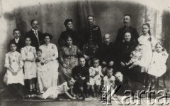 Ok. 1911, Nagy-Becskerek (obecnie Zrenjanin w Serbii), Austro-Węgry.
Zdjęcie rodzinne, w środku po obu stronach wazonu siedzą: Katalin z domu Sorg ur. 1844 r. i jej mąż Jozsef Várady, ur. w 1829. Na lewo od Katalin siedzi jej synowa Meta z domu Putz (ur. 1876, zm. 1938) i trzyma na ręku córkę Piroskę Várady (ur.1910). Nad Metą Várady stoi jej mąż Imre Várady (ur. 1867, zm. 1959). Na lewo od niego stoi Karol Sławikowski (ur. 1896, zm.1959 w Londynie). Na lewo od Mety stoi córka Mety i Imre - Hajnalka Várady, (ur. 1900), na lewo od niej druga córka Edit (ur. 1898). Nad Katalin stoi jej córka Gizella z domu Várady (ur.1871, zm. 1925 w Krakowie) obok niej stoi jej mąż Stanisław Sławikowski (ur.1866 w Tymbarku, zm.1948 w Bochni). Na prawo od Jozsefa Várady siedzi jego synowa Teréz z domu Krcselics (ur. 1884) na ręku trzyma córeczkę Katalin (ur. 1909), nad nią jej mąż Károly Várady (ur. 1869, zm. 1929). Na prawo od niego stoi Gizela Sławikowska (ur. 1898, zm. 1988 w Warszawie), niżej siedzi Helena Lilly Sławikowska (ur. 1902, zm. 1994 w Wiedniu). Najniżej od prawej strony: Eugeniusz Sławikowski (ur.1900, zginął w Katyniu 1940), Tibor Várady (syn Mety i Imre, ur. 1900, zm. 1975), Károly Várady (syn Teréz i Károly, u. 1907, zm. 1979), Erwin Sławikowski (ur.1905, zm. 1994 w Pruszkowie), Ernö Várady syn Mety i Imre , ur 1901).
Fot. NN, zbiory Ośrodka KARTA, udostępniła Elżbieta Sławikowska