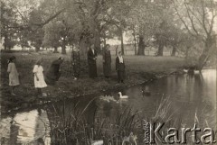 1924-1932, Kosów Poleski, woj. poleskie, Polska.
Grupa osób stojących nad brzegiem stawu i obserwujących pływające kaczki.
Fot. Feliks Drozdowski, zbiory Ośrodka KARTA, Pogotowie Archiwalne [PAF_050], udostępnił Krzysztof Drozdowski