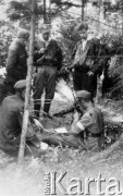 Koniec lipca 1944, Puszcza Grodzieńska, pow. Grodno.
Oddział partyzancki Bazy z Kedywu Komendy Okręgu Wileńskiego AK. Czyszczenie broni na biwaku w puszczy. Od lewej stoją: NN, prawdopodobnie Jan Leszczyński 
