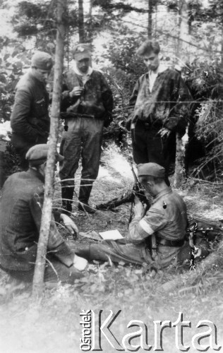 Koniec lipca 1944, Puszcza Grodzieńska, pow. Grodno.
Oddział partyzancki Bazy z Kedywu Komendy Okręgu Wileńskiego AK. Czyszczenie broni na biwaku w puszczy. Od lewej stoją: NN, prawdopodobnie Jan Leszczyński 