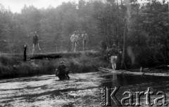 Prawdopodobnie 25.07.1944, Powosupie, Puszcza Grodzieńska, pow. Wilno-Troki.
Oddział partyzancki Bazy z Kedywu Komendy Okręgu Wileńskiego AK podczas przeprawy przez rzekę Ułę. Z prawej strony, po żerdziach idzie NN 