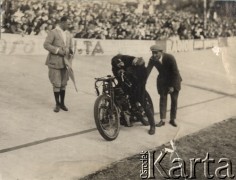 Lata 20-te lub lata 30-te, Warszawa, Polska.
Zawodnik przed startem w motocyklowym wyścigu torowym na torze na Dynasach. W tle widać reklamę proszku do prania: 
