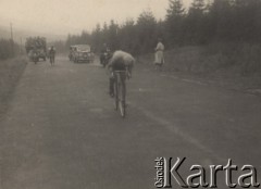 Brak daty, brak miejsca.
Kolarz na trasie wyścigu. W tle obsługa wyścigu na motorach i w samochodach.
Fot. NN, zbiory Ośrodka Karta, udostępniło Warszawskie Towarzystwo Cyklistów (WTC).
