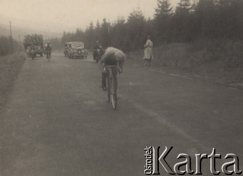 Brak daty, brak miejsca.
Kolarz na trasie wyścigu. W tle obsługa wyścigu na motorach i w samochodach.
Fot. NN, zbiory Ośrodka Karta, udostępniło Warszawskie Towarzystwo Cyklistów (WTC).