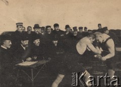 Przełom XIX i XX wieku, brak miejsca.
Pojedynek zapaśniczy, na pierwszym planie zawodnicy, na drugim publiczność, po lewej stronie stolik sędziowski.
Fot. NN, zbiory Ośrodka Karta, udostępniło Warszawskie Towarzystwo Cyklistów (WTC).