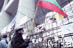 Styczeń 1991, Wilno, Litwa.
Miasto w okresie interwencji wojsk radzieckich. Mężczyzna z litewską flagą przed parlamentarnymi umocnieniami, za którymi powieszono plakaty z hasłami wolnościowymi. 
Fot. Wojciech Druszcz, zbiory Ośrodka KARTA