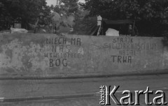 Sierpień 1980, Gdańsk, Polska.
Strajk okupacyjny w Stoczni Gdańskiej im. Lenina. Robotnicy siedzą na murze otaczającym stocznię. Na murze hasła: 