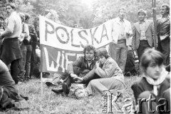 19.06.1983, Częstochowa, Polska.
Druga pielgrzymka Jana Pawła II do Polski. Wierni zgromadzeni w okolicach klasztoru paulinów na Jasnej Górze podczas mszy św. celebrowanej przez Jana Pawła II. Na trawie siedzą kobieta i mężczyzna, za nimi transparent z napisem: 