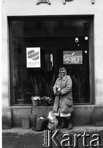 Październik 1985, Kraków, Polska
Kampania wyborcza przed wyborami do parlamentu. Kobieta handlująca kwiatami stoi przed budynkiem. W oknie wiszą plakaty z hasłami: 