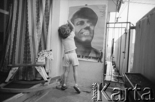 1980, Kraków, Polska.
Balkon na jednym z krakowskich osiedli. Dziecko przykleja do ściany plakat filmowy z 