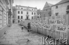 1989, Kraków, Polska
Dziewczynki biegną obok płotu z plakatami 