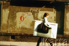 Po 1989, Kraków, Polska.
Studentka szkoły plastycznej idzie ulicą Krupniczą, mijając zamalowany farbą mur, na którym namalowano pomarańczowego krasnala - symbol wrocławskiego ruchu Pomarańczowa Alternatywa.
Fot. Piotr Dylik, zbiory Ośrodka KARTA