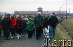 1992, Oświęcim, Polska.
KL Auschwitz Birkenau. Grupa odwiedzająca obóz. Na drugim planie uczestnicy marszu żywych. W tle wartownia i brama obozowa. 
Fot. Piotr Dylik, zbiory Ośrodka KARTA