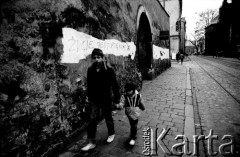 1990, Kraków, Polska.
Ulica Dominikańska. Z prawej strony Kościół Świętej Trójcy, w głębi Bazylika Franciszkanów. Na pierwszym planie chłopcy idą przy murze okalającym zespół teren kościoła Św. Józefa. Na murze napis 