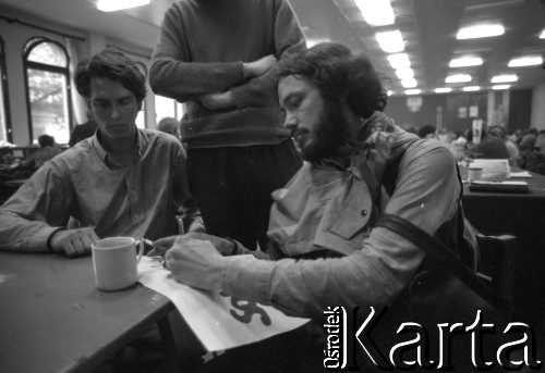 Sierpień 1980, Gdańsk, Polska.
Strajk w Stoczni Gdańskiej im. Lenina. Sala BHP, przerwa w obradach Międzyzakładowego Komitetu Strajkowego.  Mężczyźni przy stole, jeden z nich z kartką z napisem 
