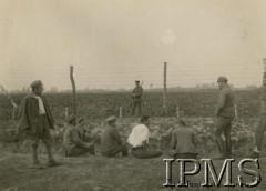 Lipiec - grudzień 1917, Szczypiorno k. Kalisza.
Żołnierze I i II Brygady Legionów, internowani w obozie jenieckim po odmowie przysięgi na wierność Niemcom. Grupa jeńców na tle ogrodzenia z drutu kolczastego, z tyłu stoi niemiecki wartownik. Podpis: 