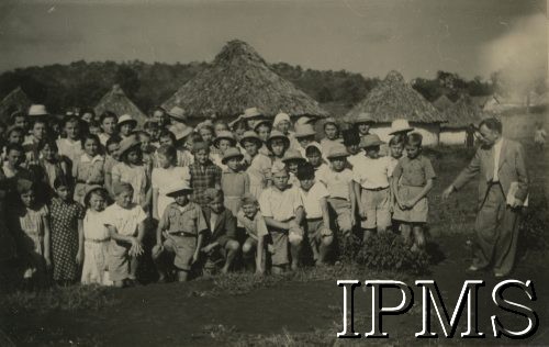 1943, Tengeru, Tanganika.
Osiedle dla polskich uchodźców, grupa uczniów.
[Polscy uchodźcy w 1942 trafili do Iranu wraz z nowoutworzonym Wojskiem Polskim pod dowództwem generała Władysława Andersa (w dwóch rzutach ewakuacyjnych z ZSRR w marcu i sierpniu). W sumie oprócz wojska dotarło tam 38 tysięcy Polaków, z czego ponad połowę stanowiły dzieci i młodzież. Ok. 20 tys. znalazło się następnie w Afryce, polskie osiedla znajdowały się przede wszystkim w: Ugandzie, Kenii, Tanganice, Rodezji Północnej i Rodezji Południowej, Związku Południowej Afryki. Tengeru było największym polskim osiedlem uchodźczym w Afryce].
Fot. NN, Instytut Polski i Muzeum im. gen. Sikorskiego w Londynie [album 288 - gen. Andersowi uchodźstwo w Afryce Wsch. 19.07.1943, w albumie dedykacja: panu generałowi Władysławowi Andersowi w imieniu uchodźstwa w Afryce inż. K. Kazimierczak, delegat MPiOS Nairobi].
