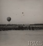 25.09.1933, Legionowo, Polska.
VI Krajowe Zawody Balonów Wolnych o Puchar im. płk. Aleksandra Wańkowicza. Większość balonów wiatr skierował na północ, w stronę niezbyt odległej granicy niemieckiej. Dlatego rekordy odległości nie były zbyt imponujące. Zwycięzcą został por. Jan Zakrzewski, który pilotował najmniejszy balon o pojemności 450 m³. Pokonując odległość 121 km, wylądował we wsi Żabiny pod Grajewem. Powyższą fotografię wykonał prawdopodobnie fotoreporter rządowy W. Pikiel. Poza balonami uwiecznił on pole wzlotów 2 Batalionu Balonowego oraz parowozownię 1 Dywizjonu Pociągów Pancernych (biały budynek w tle).
Album balonowowy - fotografie po dr Niedźwierskim.
Fot. W. Pikiel (?), Instytut Polski im. Gen. Sikorskiego w Londynie