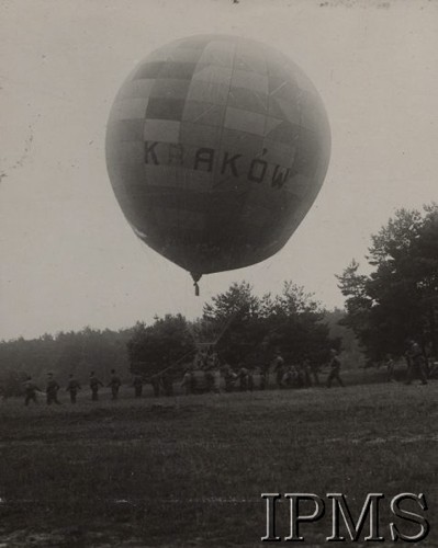 Ok. 1925, Polska.
Balon kulisty „Kraków” o pojemności 750 m³ typu „E-2” (Ballon Ecole Deux).
W grudniu 1924 r., na rozkaz komendanta Centralnego Zakładu Balonowego ppłk. Marcelego Chybczyńskiego i pod nadzorem por. Zbigniewa Burzyńskiego, biuro techniczne zakładu przystąpiło do wykonania projektu pierwszego polskiego balonu kulistego o pojemności 750 m³. 28 kwietnia 1925 r. prace zostały ukończone.  Balony te były dobrze znane pilotom wojsk balonowych, gdyż dwa z nich zakupiła w 1920 r. we Francji Polska Misja Wojskowa Zakupów. Od 1921 r. rozpoczęto na nich regularne szkolenie w Oficerskiej Szkole Aeronautycznej w Toruniu, stanowiące drugi stopień wyszkolenia w wojskach balonowych (I - obserwator balonowy, II - pilot balonów wolnych, III - pilot sterowcowy). Balon ważył 320 kg (nie licząc przyrządów i balastu) i mierzył 17,50 m wysokości. „E-2” mógł unieść dwóch, a maksymalnie trzech pilotów. W komisji opiniującej nowouszyty balon znaleźli się: jako przewodniczący kpt. Konstanty Kamieński – dowódca Detaszowanej Kompanii Balonów Zaporowych, kpt. Piotr Kamieński z Departamentu IV Żeglugi Powietrznej oraz por. Henryk Iżyłowski z Centralnego Zakładu Balonowego. 25 października 1925 r. balon „Kraków” wziął udział w I Krajowych Zawodach Balonów Wolnych o Puchar im. płk. Aleksandra Wańkowicza na Polu Mokotowskim w Warszawie. Jego załogę tworzyli wówczas kpt. Piotr Kamieński i por. Zbigniew Burzyński.
Album balonowowy - fotografie po dr Niedźwierskim.
Fot. NN, Instytut Polski im. Gen. Sikorskiego w Londynie