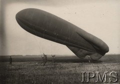 Lata 20., Polska.
Przygotowanie do wzlotu balonu zaporowego „NN”. W roku 1924 warsztat powłokowy Centralnego Zakładu Balonowego w Legionowie uruchomił produkcję pierwszych w Polsce balonów zaporowych „N”-„NN”, których licencję zakupiono we Francji. Ich szycie rozpoczęto na początku sierpnia 1924 r.   Balony „N”-„NN”, systemu „Caquot DCA” (Defense Contre Aeronefs – OPL), skonstruował francuski oficer – mjr inż. Albert Caquot. Balony były używane po dwa. W celu zwiększenia pułapu operacyjnego łączono je w tandem (jeden nad drugim), połączony stalową liną. Teoretycznie osiągał on pułap 4500 m, ale w rzeczywistości po uwzględnieniu kąta znoszenia był niższy o 700 m. Balon „NN” (górny) o długości 17,3 m osiągał objętość ok. 288 m³. Balony „N”-„NN” były ówcześnie jednymi z najnowocześniejszych na świecie. Mjr A. Caquot zastosował w nich nietypowy sposób wyrównywania gazu w powłoce, którego objętość rozszerzała się wraz z wysokością. W tym celu wbudował w powłokę, widoczny na powyższym zdjęciu, gumowy pas rozszerzalny.
Album balonowowy - fotografie po dr Niedźwierskim.
Fot. NN, Instytut Polski im. Gen. Sikorskiego w Londynie