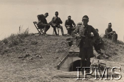 Po 22.06.1941, brak miejsca.
Punkt dowodzenia jednej z jednostek 1 Dywizji Strzelców Górskich. Na pierwszym planie - oficer z lornetką i torbą meldunkową na ramieniu. Na mundurze oficera widoczny jest Krzyż Żelazny I Klasy. Na drugim planie żołnierze siedzący na krzesłach oraz aparat fotograficzny.
Fot. NN, Instytut Polski i Muzeum im. gen. Sikorskiego w Londynie