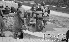 Maj 1944, Cassino, Włochy.
Rodzajowa scena na ulicy - grupa osób przy studni, obok stoi motocykl, który naprawia motocyklista.
Fot. por. Ostrowski, Instytut Polski im. Gen. Sikorskiego w Londynie [album negatywowy L-II Monte Cassino] - płachta 6