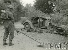 19.08.1944, okolice Chambois, Francja.
I Dywizja Pancerna pod Chambois. Na pierwszym planie saper z wykrywaczem metali, w tle rozbity samochód i zwłoki żołnierza.
Fot. por. M. Barchólski, Instytut Polski i Muzeum im. gen. Sikorskiego w Londynie
