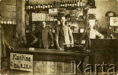 Ok. 1914-1918, brak miejsca.
Obsługa kantyny batalionu zapasowego 59 Rezerwowego Pułku Piechoty. Za ladą stoją sierżant oraz dwóch szeregowców armii niemieckiej. Na ladzie tablica z napisem w języku niemieckim: 