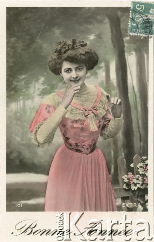 1907, Francja.
Portret kobiety w różowej sukni na tle lasu. Zdjęcie wykonane w atelier fotograficznym. W prawym górnym rogu naklejony znaczek pocztowy o wartości 5C, z napisiem 