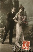 Pocz. XX wieku, Francja.
Portret zakochanej pary - kobiety w sukni, z naszyjnikiem z pereł, diademem we włosach oraz mężczyzny w ciemnym garniturze. Kobieta trzyma w dłoniach bukiet kwiatów. Zdjęcie wykonane w atelier fotograficznym. Na odwrocie tekst w języku francuskim.
Fot. NN, zbiory Ośrodka KARTA, kolekcja Ryszarda Łopatki