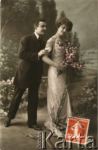 Pocz. XX wieku, Francja.
Portret zakochanej pary - kobiety w sukni, z naszyjnikiem z pereł, diademem we włosach oraz mężczyzny w ciemnym garniturze. Kobieta trzyma w dłoniach bukiet kwiatów. Zdjęcie wykonane w atelier fotograficznym. Na odwrocie tekst w języku francuskim.
Fot. NN, zbiory Ośrodka KARTA, kolekcja Ryszarda Łopatki