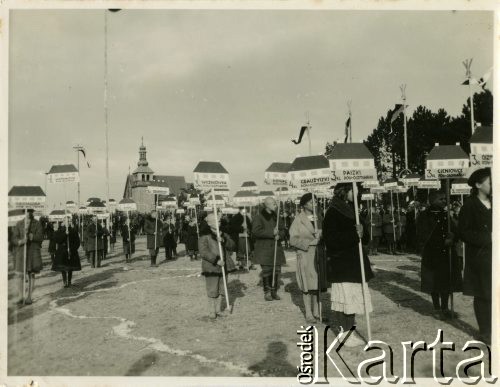 Lipiec 1937, Bezdany, woj. wileńskie, Polska. 
Uroczyste poświęcenie nowo wybudowanej szkoły. Po śmierci Marszałka Józefa Piłsudskiego rząd polski ogłosił rozporządzenie wybudowania 100 szkół w woj. wileńskim. Na zdjęciu pochód ludzi, którzy trzymają tablice z nazwami miejscowości, w których wybudowano nowe szkoły.
Fot. Jerzy Konrad Maciejewski, zbiory Ośrodka KARTA