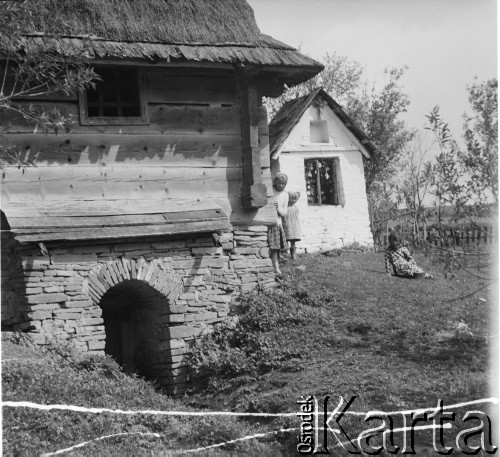 Lata 50., Bieszczady, Polska.
Dzieci przy drewnianym domu. W głębi widać białą murowaną kapliczkę.
Fot. Jerzy Konrad Maciejewski, zbiory Ośrodka KARTA.