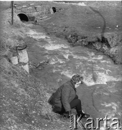 Marzec 1967, Duszniki-Zdrój, woj. wrocławskie, Polska.
Kobieta siedzi nad brzegiem rzeki Bystrzyca Dusznicka.
Fot. Jerzy Konrad Maciejewski, zbiory Ośrodka KARTA