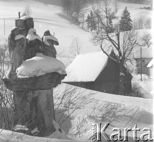 Lata 60., Duszniki-Zdrój, woj. wrocławskie, Polska.
Przydrożna kaplica zasypana śniegiem. W głębi widoczne domy górskie.
Fot. Jerzy Konrad Maciejewski, zbiory Ośrodka KARTA