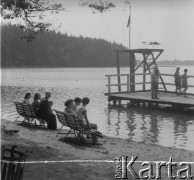 1961 lub 1965, Wigry, woj. białostockie, Polska.
Turyści wypoczywają  na plaży nad jeziorem Wigry. Na zdjęciu widoczny pomost ze stanowiskiem dla ratownika. 
Fot. Jerzy Konrad Maciejewski, zbiory Ośrodka KARTA