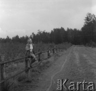 Lata 60. lub 70., Górecko Kościelne, woj. lubelskie, Polska.
Kobieta pozuje do zdjęcia siedząc na ogrodzeniu przy drodze. 
Fot. Jerzy Konrad Maciejewski, zbiory Ośrodka KARTA