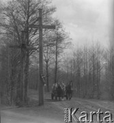 Lata 60. lub 70., Górecko Kościelne, woj. lubelskie, Polska.
Mężczyzna na wozie zaprzęgniętym w dwa konie mija przydrożny, drewniany krzyż.
Fot. Jerzy Konrad Maciejewski, zbiory Ośrodka KARTA