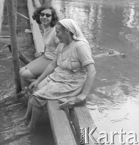 Lata 60. lub 70., Górecko Kościelne, woj. lubelskie, Polska.
Kama Nowak z Sofii (z lewej) i Maria Krzeszowcowa z Górecka Kościelnego siedzą na kładce nad rzeką Szum.
Fot. Jerzy Konrad Maciejewski, zbiory Ośrodka KARTA