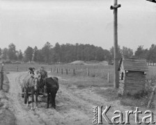 Lata 60. lub 70., Górecko Kościelne, woj. lubelskie, Polska.
Mężczyzna na wozie zaprzęgniętym w dwa konie mija przydrożny krzyż, obok którego stoi mała, drewniana kaplica.
Fot. Jerzy Konrad Maciejewski, zbiory Ośrodka KARTA