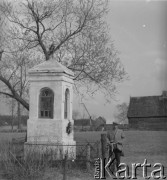 Lata 60. lub 70., Górecko Kościelne, woj. lubelskie, Polska.
Mężczyzna z rowerem stoi przy przydrożnej, murowanej kaplicy.
Fot. Jerzy Konrad Maciejewski, zbiory Ośrodka KARTA