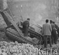 Po 1945, Warszawa, Polska.
Robotnicy stoją wokół leżącej w gruzach maszyny. Wokół widoczne zniszczone kamienice.
Fot. Jerzy Konrad Maciejewski, zbiory Ośrodka KARTA
